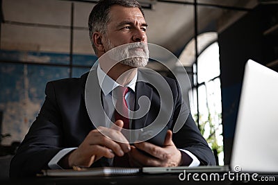 Mature business man in formal clothing using mobile phone. Serious businessman using smartphone and laptop at work Stock Photo
