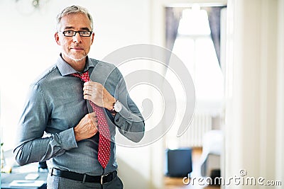Mature businessman on a business trip standing in a hotel room, getting dressed. Stock Photo