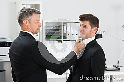 Mature Businessman Gripping Employee's Tie Stock Photo