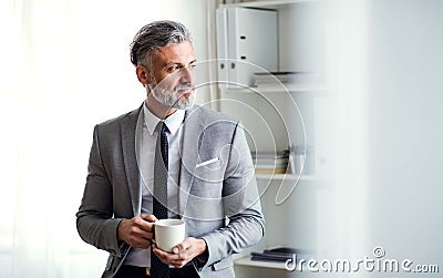 A mature businessman standing in an office, holding a cup of coffee. Copy space. Stock Photo