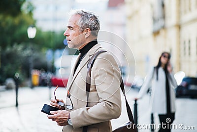Mature businessman standing on a street in city, holding glasses. Stock Photo