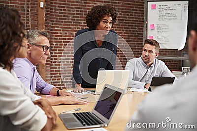 Mature Businesswoman Standing And Leading Office Meeting Around Table Stock Photo