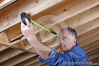 Mature construction worker measuring distance between rafter beams. Stock Photo