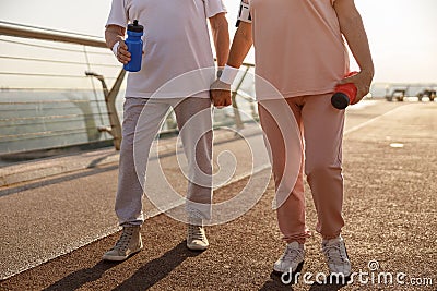 Mature couple in sportswear with bottles stands on city footbridge in evening Stock Photo