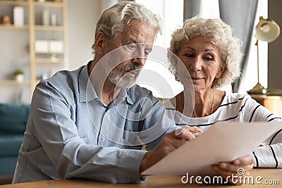 Mature couple read medical insurance terms seated at table indoors Stock Photo