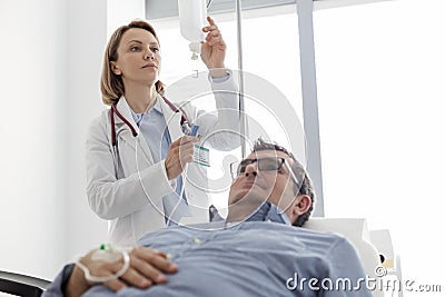 Mature doctor adjusting saline IV drip for patient in hospital ward Stock Photo