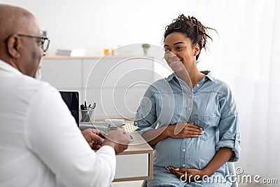 Mature experienced black doctor showing pills to pregnant lady Stock Photo