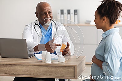 Mature experienced black doctor showing pills to pregnant lady Stock Photo