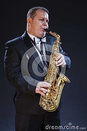 Mature Expressive Caucasian Saxophonist in Dark Suit Posing Against Seamless Black Background Stock Photo