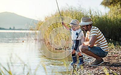 A mature father with a small toddler son outdoors fishing by a lake. Stock Photo