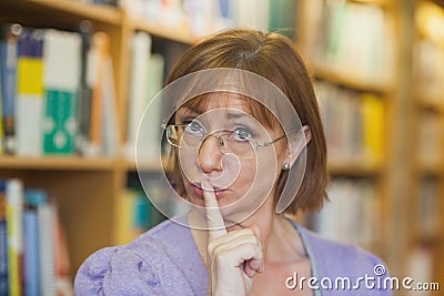 Mature female librarian giving a sign to be quiet standing in library Stock Photo