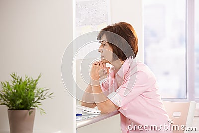 Mature female office worker thinking at desk Stock Photo