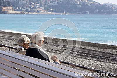 A mature, gray-haired beautiful couple: a man and a woman are sitting on a white bench on the Promenade des Anglais and looking at Editorial Stock Photo