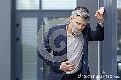 Mature gray haired boss has food poisoning, man outside office building has severe stomach pain and nausea, boss is Stock Photo