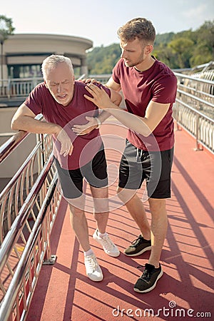 Mature grey-haired male holding his hand on chest, young male helping him Stock Photo