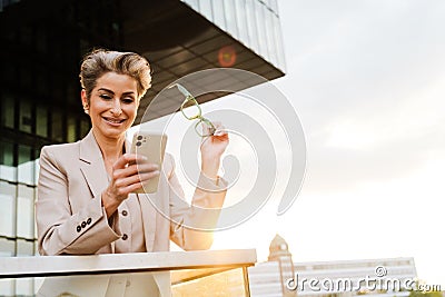 Mature grey woman smiling and using mobile phone on balcony Stock Photo