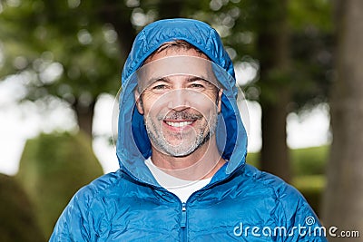 Mature handsome man wearing windbreaker with hood on smiling at the camera. Outside. Stock Photo