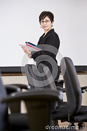 Mature Hispanic business woman standing by chairs Stock Photo