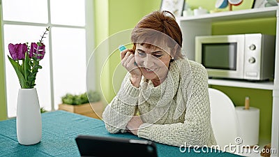 Mature hispanic woman holding vape inhaler sitting on table watching video on touchpad at dinning room Stock Photo