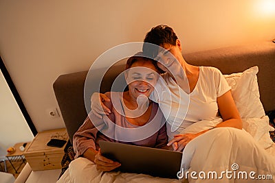 Mature lesbian couple hugging and using laptop in bed Stock Photo