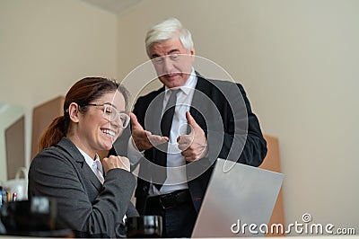 A mature male boss praises a subordinate. A woman in a suit works at a laptop at a desk. Friendly colleagues chat in the Stock Photo