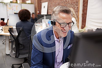 Mature Male Customer Services Agent Working At Desk In Call Center Stock Photo