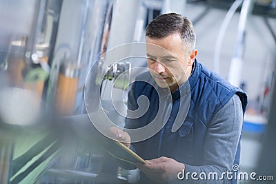 Mature male inspector writing on clipboard in factory Stock Photo