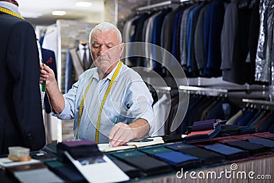 Mature male tailor takes measurement from his jacket using measuring tape Stock Photo