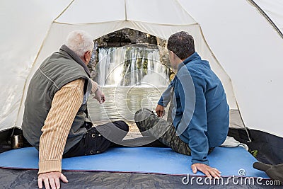 Mature male tourists sit in a tent and admire the beautiful Atysh waterfall Stock Photo