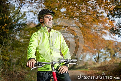 Mature Man Cycling Along Autumn Country Road Stock Photo