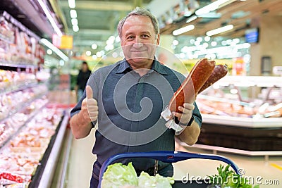 Mature man diligently choosing tasty sausage in supermarket Stock Photo