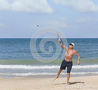 A mature man hits a ball while playing matkot on the beach Stock Photo