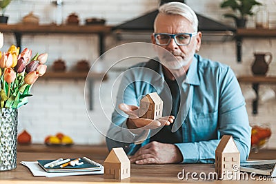 A mature man holds a miniature house in his hands. Loss of money on unprofitable property purchases Stock Photo