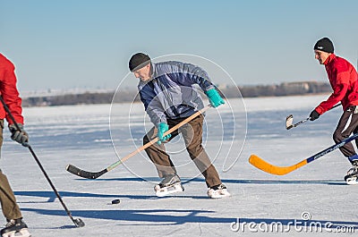 Mature man leading pack while playing hockey on a frozen river Editorial Stock Photo