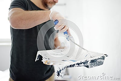 Mature man making repairs in the apartment. The person paints the wall white with roller. Do it yourself. DIY Stock Photo