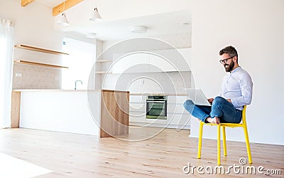 A mature man sitting on chair in unfurnished new house, using laptop. Stock Photo