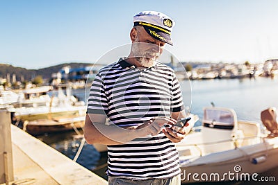 Man standing near the sea dressed in a sailor`s shirt and hat using smart phone Stock Photo