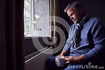 Mature Man Trying To Keep Warm By Radiator At Home During Cost Of Living Energy Crisis Stock Photo
