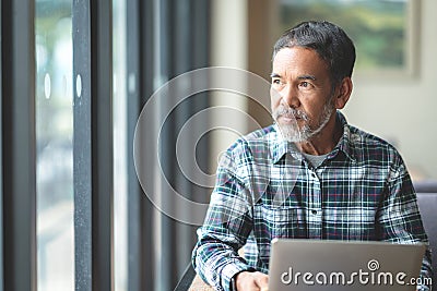 Mature man with white stylish short beard looking outside window. Casual lifestyle of retired hispanic people Stock Photo