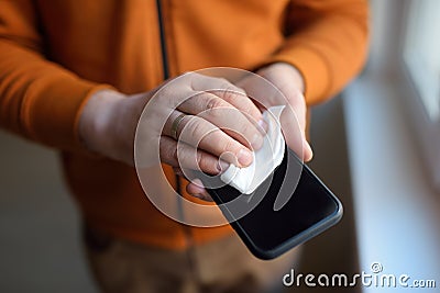 Mature man wipes with a disinfecting cloth heis smartphone after returning home. Safety during COVID-19 outbreak in public places Stock Photo