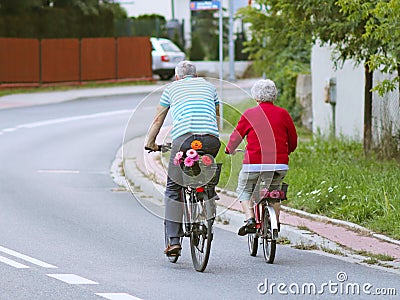 Mature man and woman rides a bicycle among the greens. A healthy and active part of life. Ecological transport for the population. Editorial Stock Photo