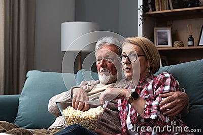 Mature married couple entertaining observing terrified TV program. Senior husband and wife watching horror movie or film at home Stock Photo