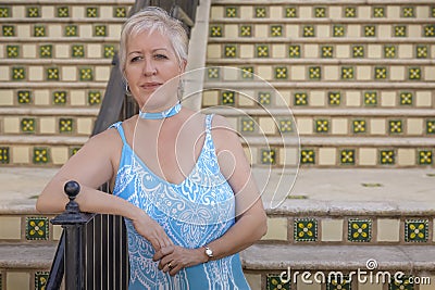 A mature modern blond woman waits at the bottom of the steps leaning on the rail Stock Photo