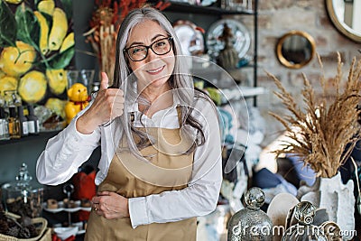 Mature saleswoman smiling and showing thumb up at shop Stock Photo