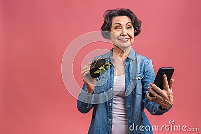 Mature senior woman eating burger with satisfaction. Grandmother enjoys tasty hamburger takeaway, delicious bite of burger, using Stock Photo