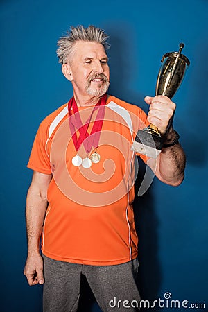 Mature sportsman with medals holding trophy cup on blue Stock Photo