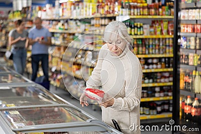 Mature woman choosing frozen food in supermarket. Young woman purchasing goods in grocery store Stock Photo