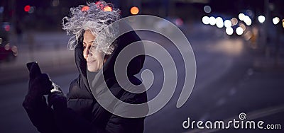 Mature Woman On City Street At Night Ordering Taxi Using Mobile Phone App Stock Photo