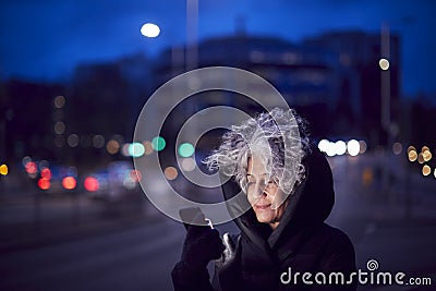 Mature Woman On City Street At Night Ordering Taxi Using Mobile Phone App Stock Photo