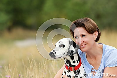 Mature woman is cuddling a dalmatian dog in a meadow outdoor Stock Photo